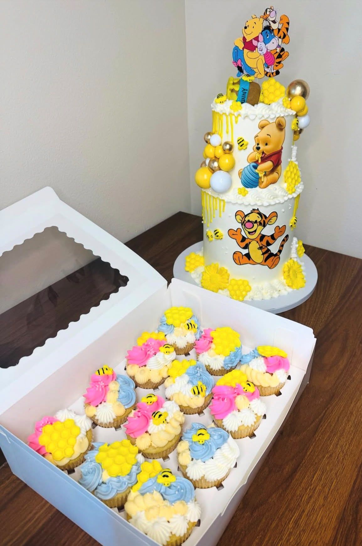 Caja de cupcakes decorados con abejitas y panales junto a tarta de Winnie the Pooh